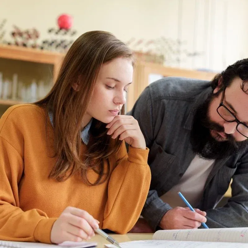 Standard English female student working on homework while an experienced tutor looks over.